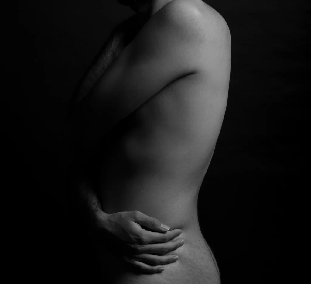 Photo d'un corps d'homme nu qui entoure son corps avec ses bras. L'image est en noir et blanc.