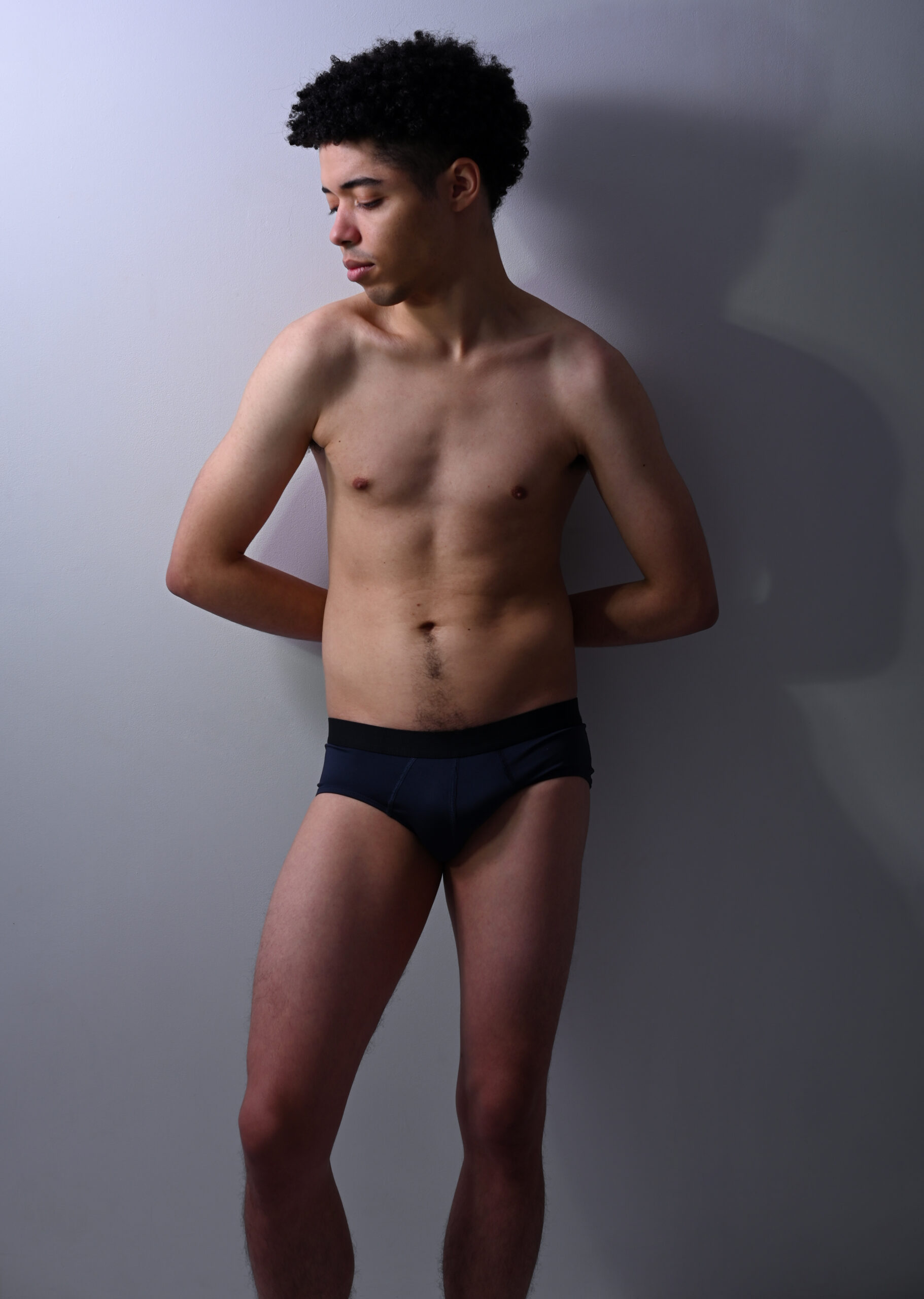 Un modèle homme en slip pose contre un mur