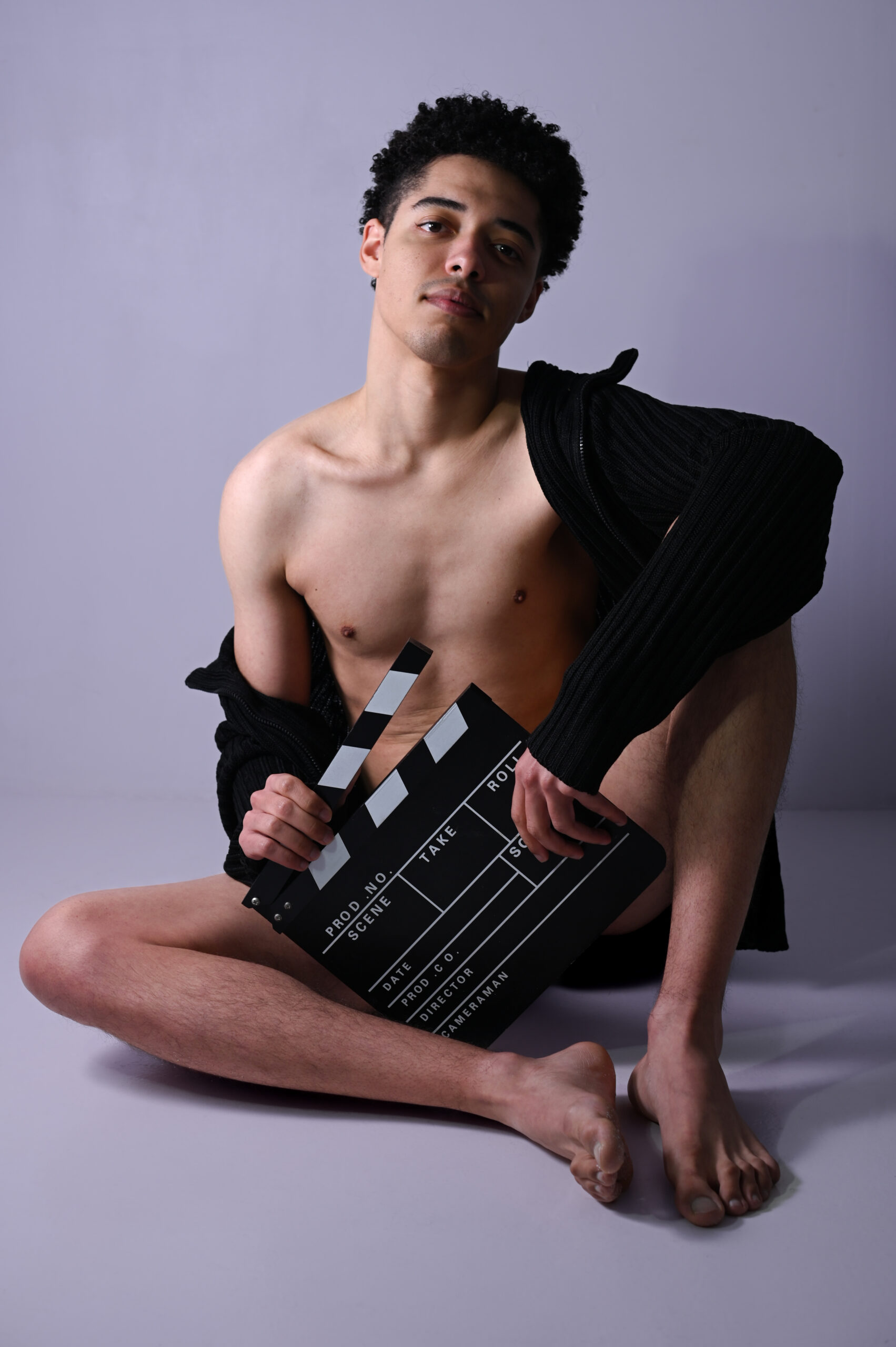 Un modèle masculin nu assis avec un clap de cinéma entre les jambes